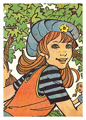 Smiling girl with red hair wearing a blue striped hat and orange vest in front of tree leaves.