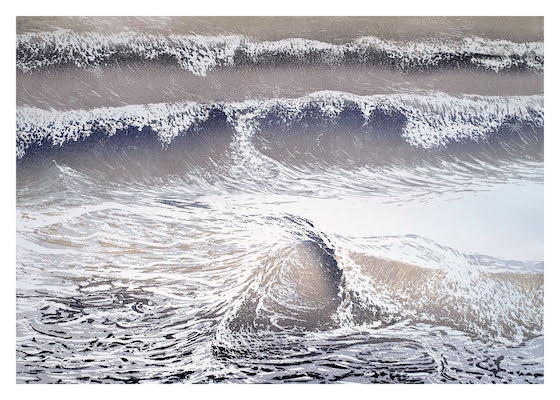 Aerial view of foamy ocean waves breaking and rolling toward a sandy shore.