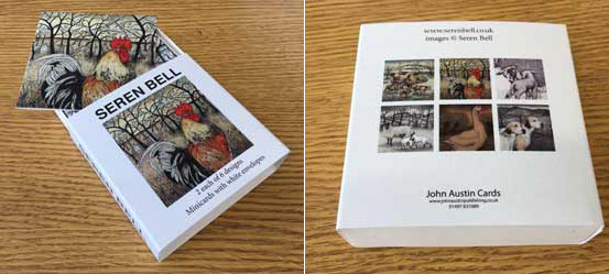 Box of Seren Bell notecards featuring rooster and hen artwork on a wooden surface.